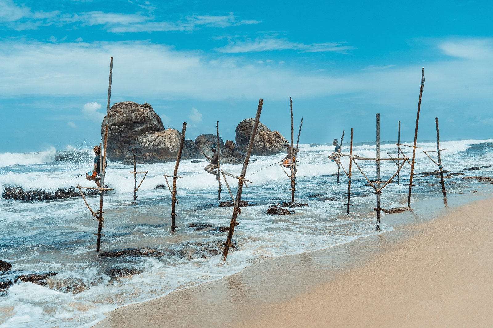 Traditional fishing sticks on the beach with rocks and waves in the background.